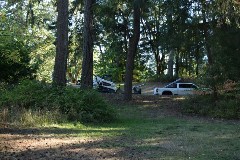 Pickup truck and skid steer preparing a level site for Derksen shed delivery in Dickson, Tennessee wooded backyard.